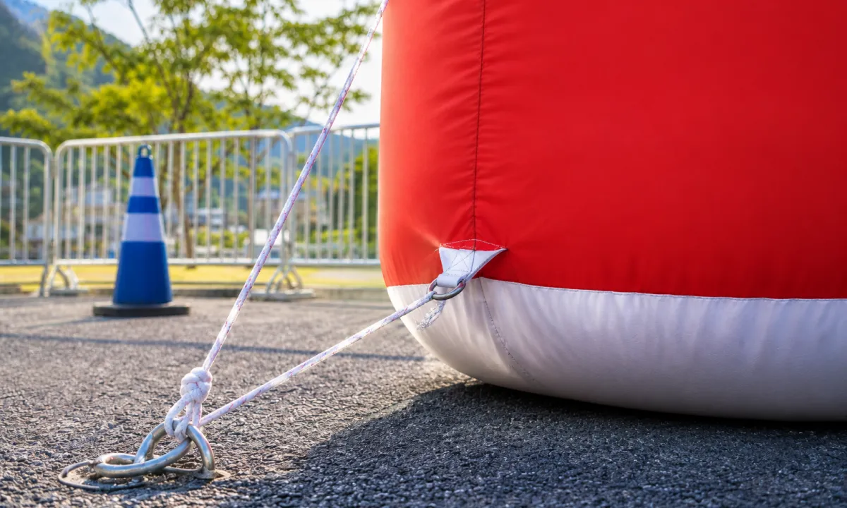 Tether rope from the base D-ring of a large inflatable secured to a ground anchor on asphalt — how to tie down inflatables on hard surfaces